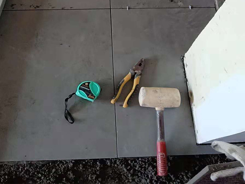 客廳地磚鋪貼：鋪貼的工具包括橡膠錘和粘結(jié)劑。在進(jìn)行施工之前先把所需要的這些材料都整理好放在一旁備用；基層的處理工作對(duì)瓷磚的平整度有很大的影響，對(duì)于基層要做好清潔工作，還有找平工作。放樣：在進(jìn)行瓷磚的鋪貼工作之前還事先找好垂直線，這樣可以在鋪貼的時(shí)候找到瓷磚的水平線，讓瓷磚鋪貼的更加的平整。粘結(jié)劑加水?dāng)嚢杈鶆?，靜置10分鐘之后就可以使用。將瓷磚表面的浮灰清除，再在瓷磚背面均勻的涂抹上粘結(jié)劑，按照預(yù)鋪的順序?qū)⒋纱u鋪貼在地面上，最后用橡膠錘輕輕拍打至服帖齊整。