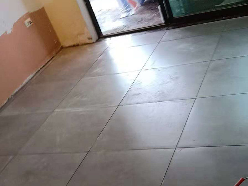 客廳地磚鋪貼：鋪貼的工具包括橡膠錘和粘結(jié)劑。在進(jìn)行施工之前先把所需要的這些材料都整理好放在一旁備用；基層的處理工作對(duì)瓷磚的平整度有很大的影響，對(duì)于基層要做好清潔工作，還有找平工作。放樣：在進(jìn)行瓷磚的鋪貼工作之前還事先找好垂直線，這樣可以在鋪貼的時(shí)候找到瓷磚的水平線，讓瓷磚鋪貼的更加的平整。粘結(jié)劑加水?dāng)嚢杈鶆?，靜置10分鐘之后就可以使用。將瓷磚表面的浮灰清除，再在瓷磚背面均勻的涂抹上粘結(jié)劑，按照預(yù)鋪的順序?qū)⒋纱u鋪貼在地面上，最后用橡膠錘輕輕拍打至服帖齊整。
